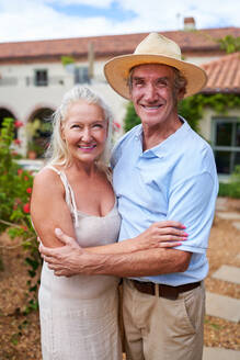 Portrait happy senior couple hugging in villa garden - CAIF33821