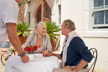 Waiter serving coffee to happy senior couple at sidewalk cafe table - CAIF33830