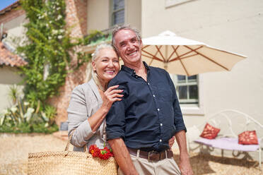 Portrait happy senior couple hugging on sunny summer villa patio - CAIF33834