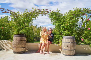 Happy senior couple drinking cocktails under trellis on sunny patioid - CAIF33853