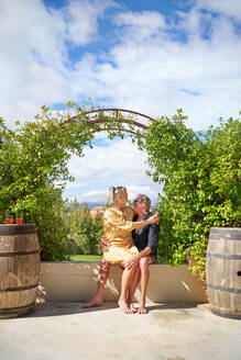 Affectionate senior couple hugging under trellis on sunny patio - CAIF33854