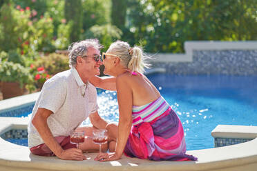 Happy, affectionate senior couple kissing and drinking at swimming pool - CAIF33862