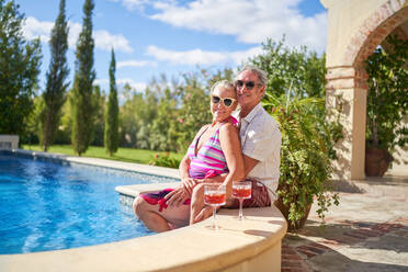 Portrait happy senior couple relaxing at sunny summer swimming pool - CAIF33867
