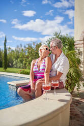 Affectionate senior couple talking at sunny summer swimming pool - CAIF33868