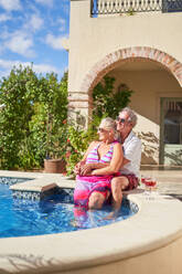 Carefree senior couple relaxing at swimming pool on villa patio - CAIF33870