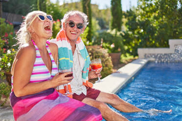 Portrait happy, carefree senior couple laughing at summer swimming pool - CAIF33878
