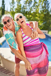 Portrait happy, playful senior couple hugging at sunny poolside - CAIF33880