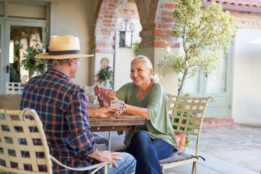 Happy senior couple playing card game at villa patio table - CAIF33885