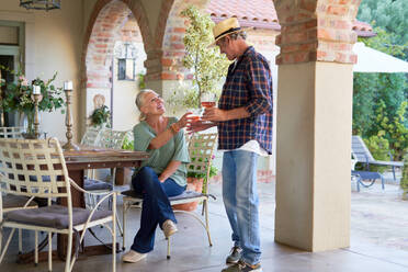 Happy senior couple drinking cocktails on villa patio - CAIF33886