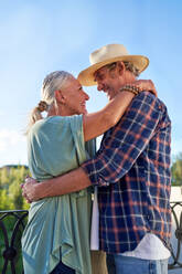 Happy, affectionate senior couple hugging on balcony - CAIF33892