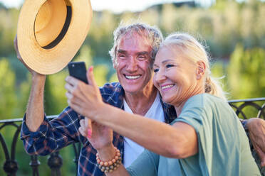 Happy senior couple taking selfie on balcony - CAIF33896