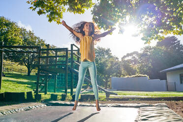 Carefree girl jumping on trampoline in sunny backyard - CAIF33908