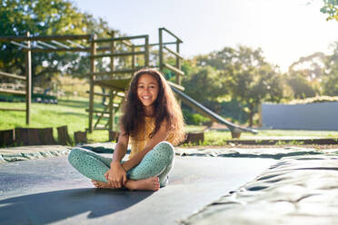 Portrait carefree girl sitting on trampoline in sunny backyard - CAIF33909