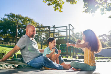 Father and children sitting on trampoline in sunny backyard - CAIF33910