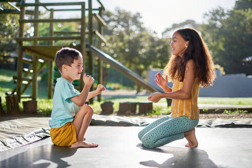 Happy brother and sister playing clapping game on sunny trampoline - CAIF33911