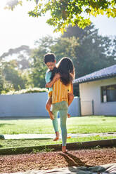 Sister carrying cute brother in sunny summer backyard - CAIF33912
