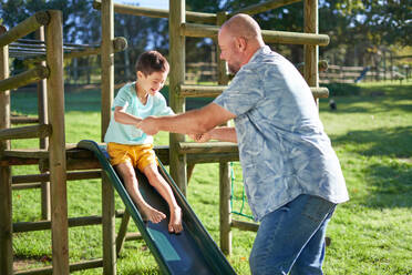 Father playing with son with Down Syndrome on slide in sunny backyard - CAIF33913