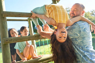 Father holding daughter upside-down, playing in sunny backyard - CAIF33921