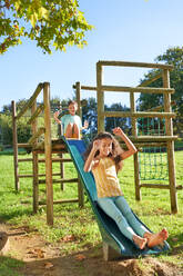 Carefree brother and sister playing on slide at playground structure - CAIF33924