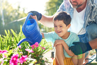 Portrait happy boy with Down Syndrome watering flowers with father - CAIF33932