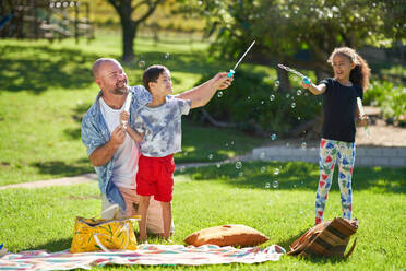 Happy family playing with bubbles in sunny summer park - CAIF33950