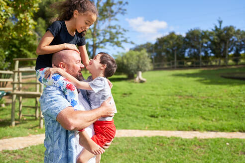 Father holding cute, playful kids in sunny summer park - CAIF33959