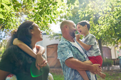 Happy parents and son with Down Syndrome below sunny tree - CAIF33963