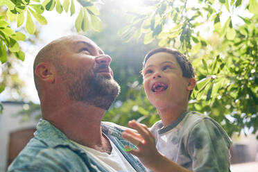 Close up happy father and son with Down Syndrome below tree - CAIF33964