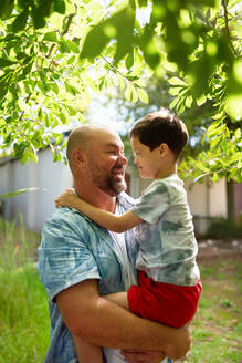 Happy father holding cute son with Down Syndrome in backyard - CAIF33967