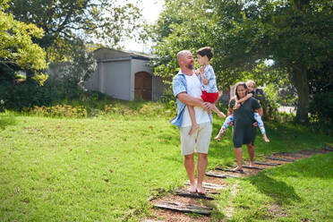 Happy parents carrying daughter and son on path in sunny backyard - CAIF33968