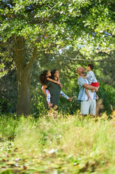 Happy family standing below tree in sunny summer park - CAIF33969