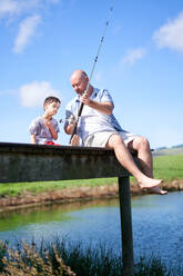 Father teaching son with Down Syndrome fishing on summer dock - CAIF33973