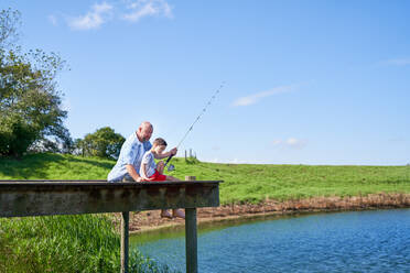 Father and son fishing on sunny summer lakeside dock - CAIF33976