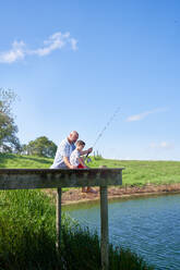 Father and son fishing on sunny summer lakeside dock - CAIF33977