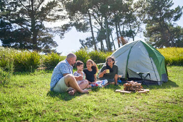 Happy family talking and drinking outside tent at sunny summer campsite - CAIF33983