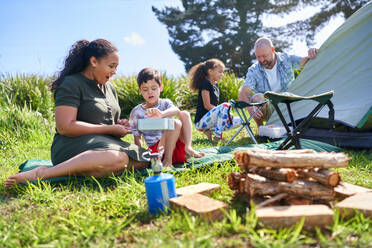 Family cooking and pitching tent at sunny summer campsite - CAIF33987