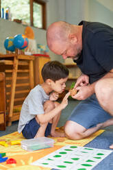 Father teaching son with Down Syndrome about plants at home - CAIF33991