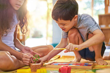 Sister watching brother with Down Syndrome playing with toys on floor - CAIF33999