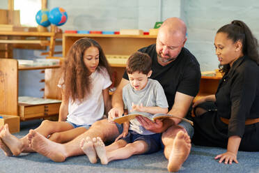 Barefoot family reading book on floor at home - CAIF34002