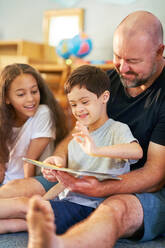 Cute boy with Down Syndrome reading book with family at home - CAIF34004