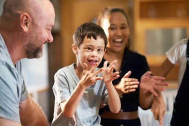 Portrait happy boy with Down Syndrome clapping with family - CAIF34010