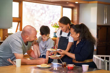 Happy family eating pancakes in morning kitchen - CAIF34018