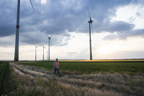 Ingenieur auf einem landwirtschaftlichen Feld mit Windturbinen vor dem Himmel - UUF29272