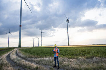 Engineer using tablet PC on wind field in front of sky - UUF29274