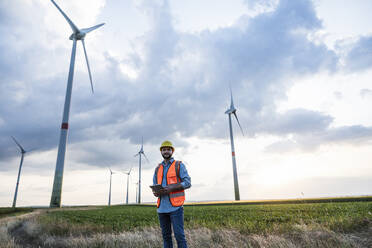 Engineer holding tablet PC on wind field in front of sky - UUF29275