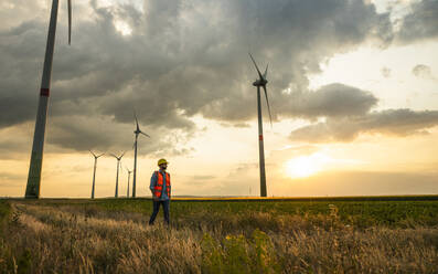 Ingenieur in reflektierender Kleidung auf einem Feld bei Sonnenuntergang - UUF29278