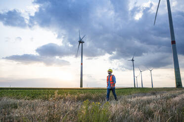 Engineer walking on grass at wind farm - UUF29279