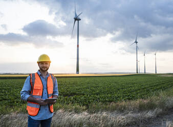 Engineer holding tablet PC standing at wind farm - UUF29281