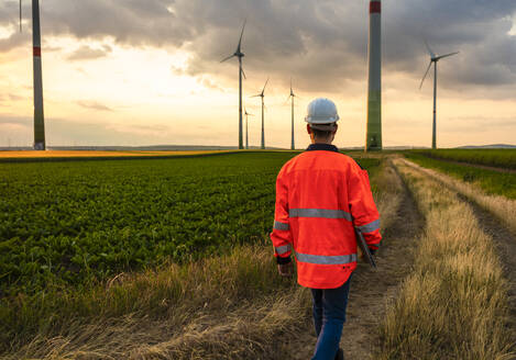 Ingenieur in reflektierender Kleidung geht auf Windkraftanlagen zu - UUF29285