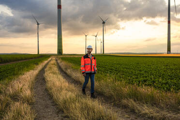 Engineer in reflective clothing walking with laptop at wind farm - UUF29286